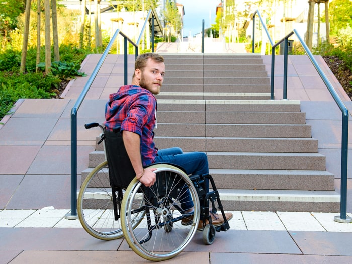 Behinderter Mann im Rollstuhl vor einer Treppe